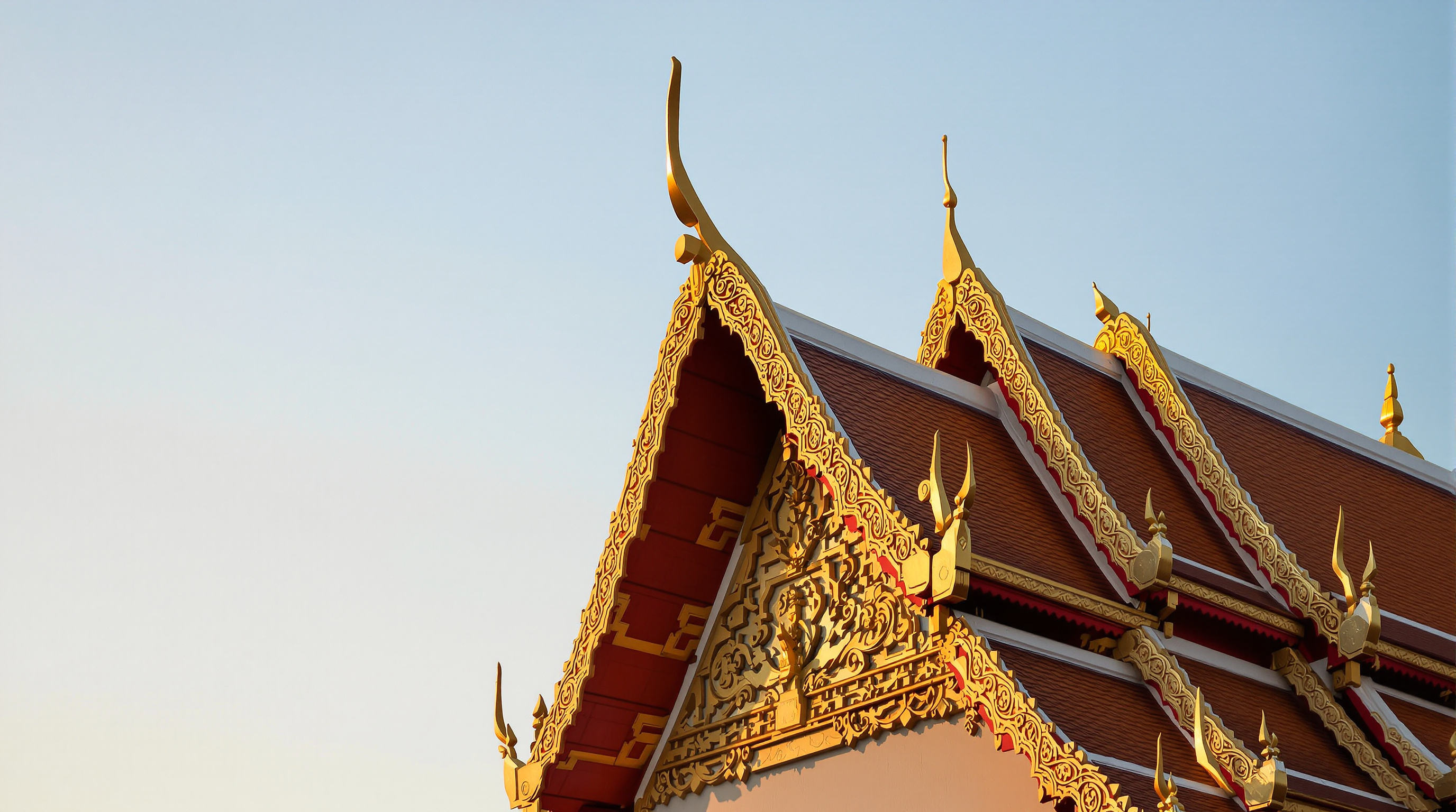 The ornate golden gable of an old Thai temple against a clear sky at golden hour