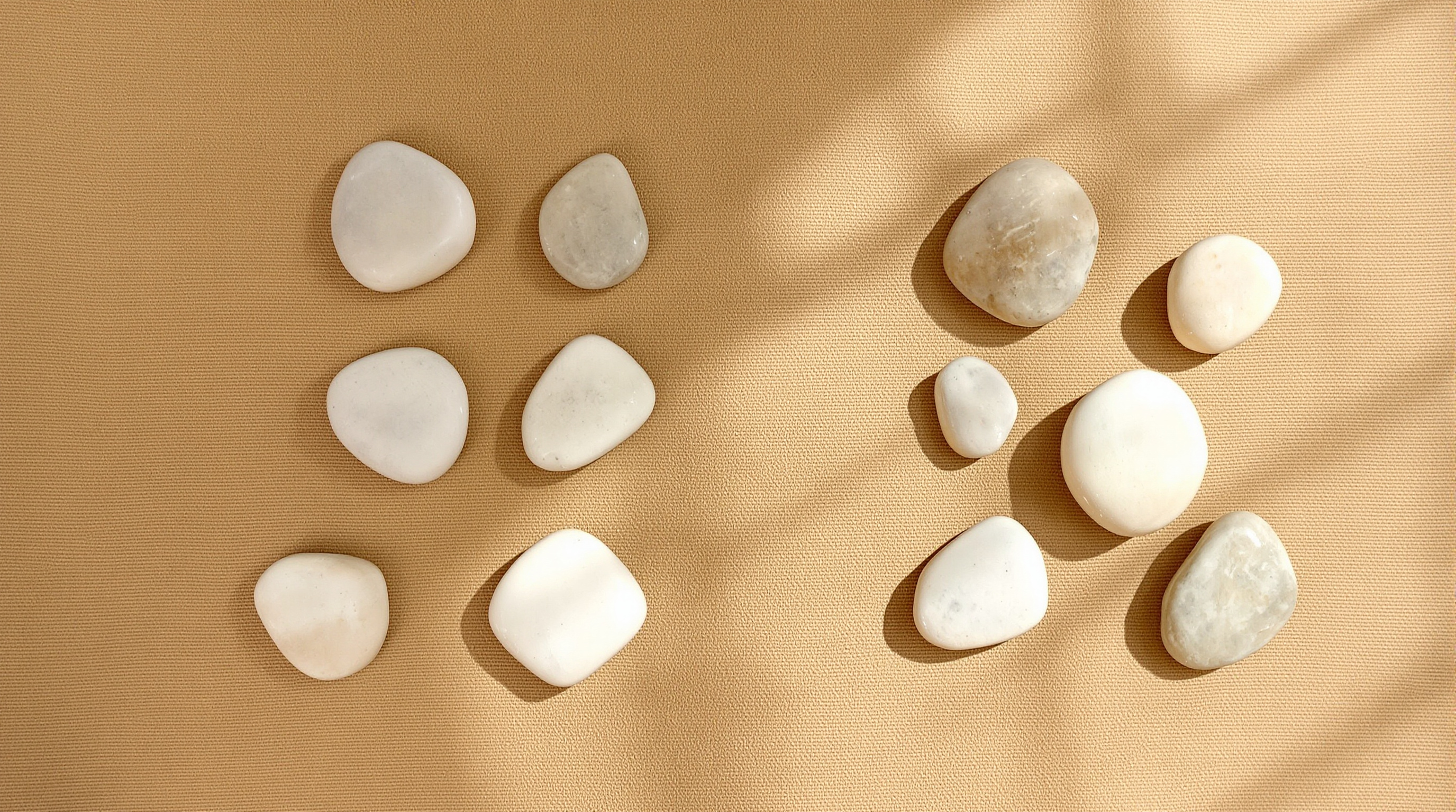 Pale river pebbles laid out in two separate clusters on sand-coloured cloth in raking sunlight
