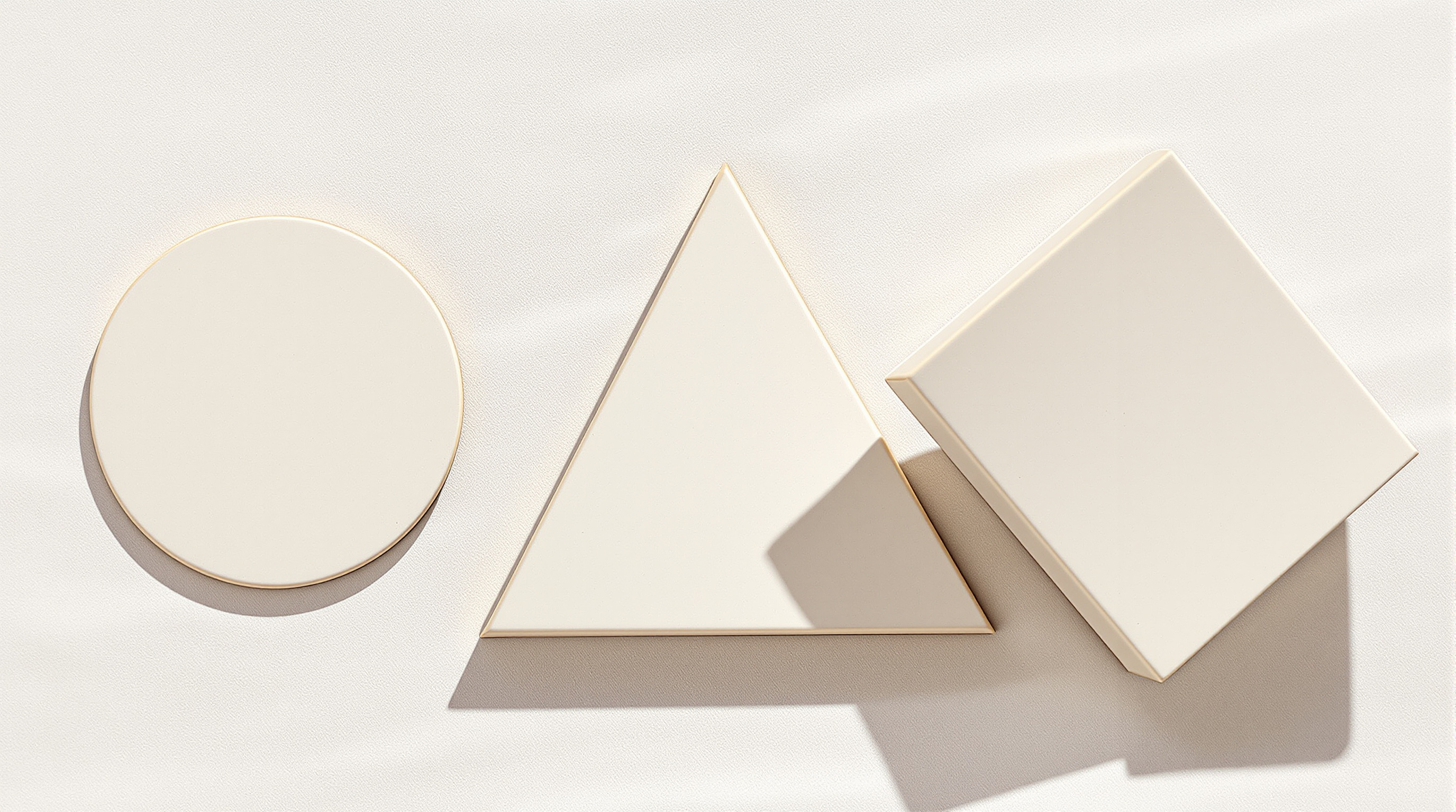 A plain circle, a triangle and a tilted square in cream card laid out on a white surface under soft light